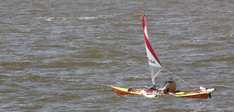 A single sea kayak equipped with a Hobie sail and amas.