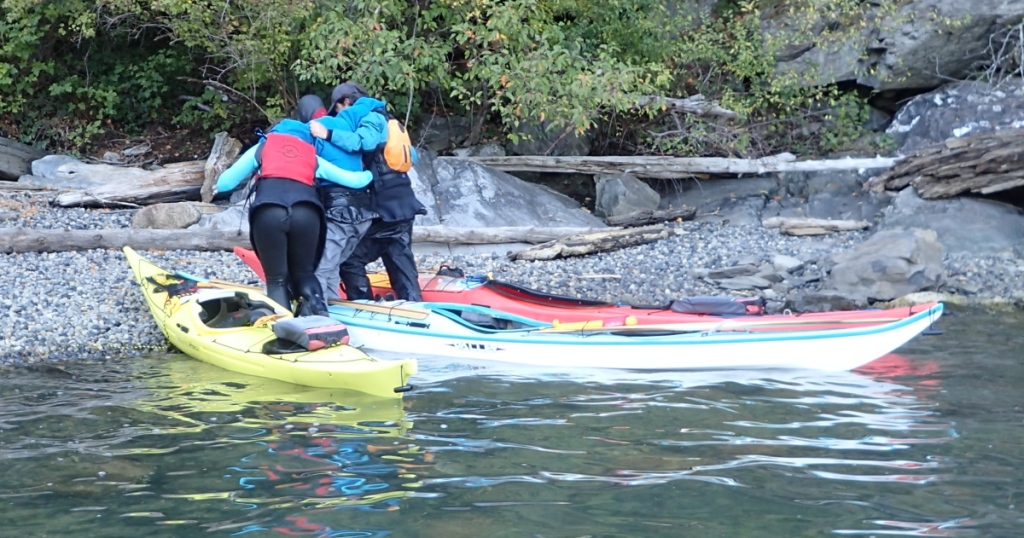 sea kayak rescue practice: rescuers help a simulated hypothermia victim out of her boat and onto the shore