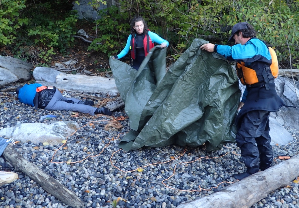 sea kayak rescue training: as a simulated hypothermia victim waits in the recovery position, two rescuers lay out a "burrito" for rewarming her.
