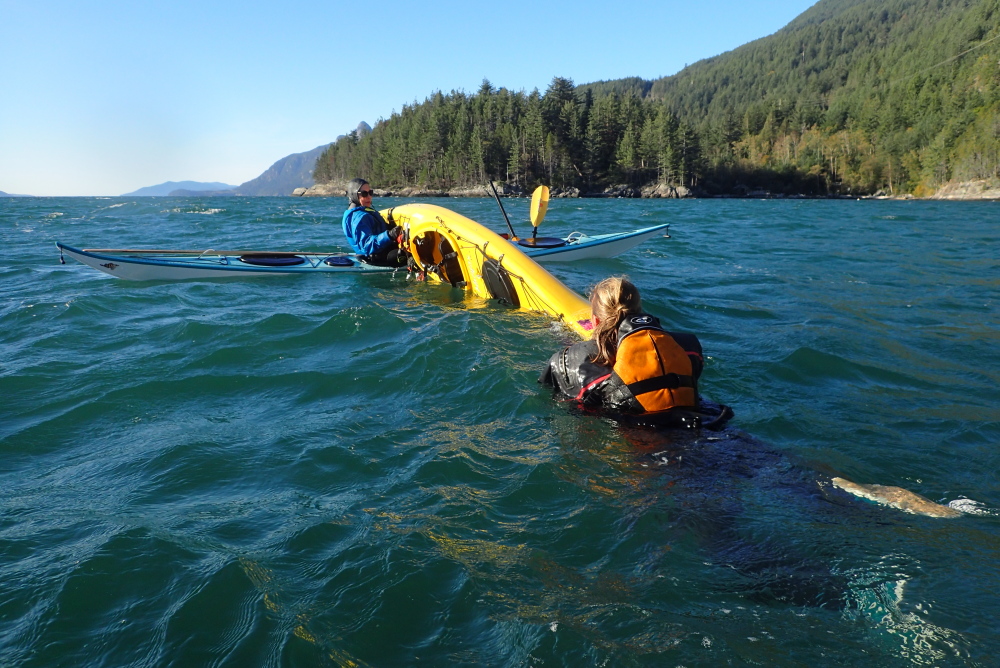 sea kayak rescue practice: one kayaker uses the T-rescue technique to empty the boat of a capsized paddler prior to helping them reboard.